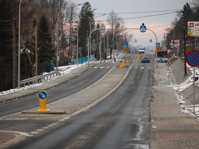 Zdjęcie przedstawiające ulicę z wyspą rozdzielającą pasy ruchu i znakami przejścia dla pieszych zimą.