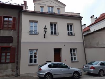 Zdjęcie przedstawiające niewielką kamienicę z jasną elewacją przy pl. św. Mikołaja 12 i zaparkowanymi przed nią samochodami