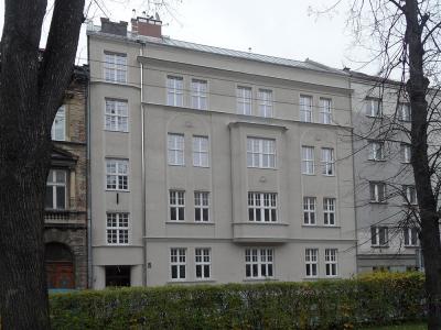 Zdjęcie przedstawiające odnowioną kamienicę z jasną elewacją, częściowo zasłoniętą drzewami.