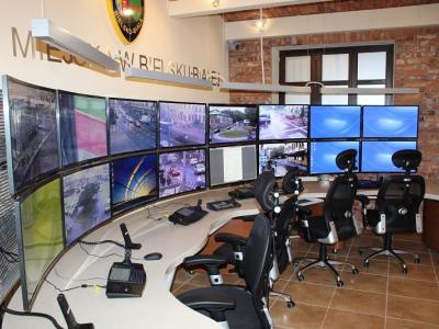 Zdjęcie przedstawiające stanowisko monitoringu miejskiego z wieloma ekranami i krzesłami.