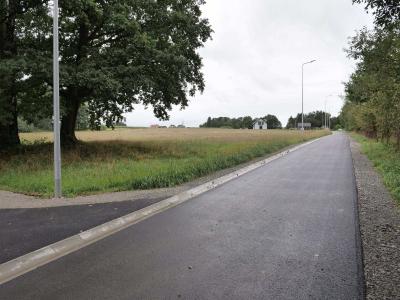 Zdjęcie przedstawiające nową asfaltową drogę biegnącą wzdłuż pola i drzew.